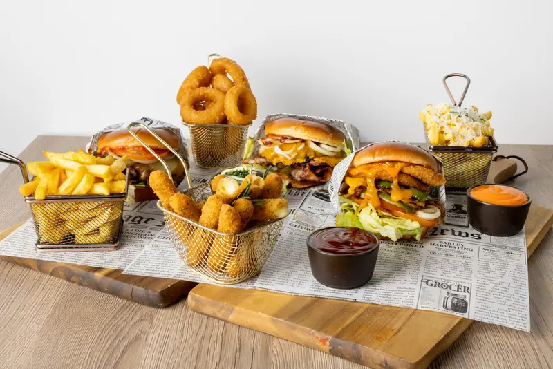 Burger, Pommes, Onion Rings und Mozzarella Sticks von Le Bistro Foodtruck auf Zeitungspapier und Holzbrett